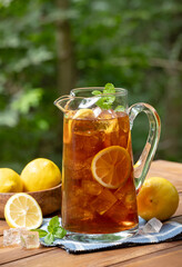 Pitcher of ice tea with lemon slices and mint outdoors on wooden table