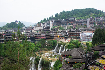 Obraz premium Cityscape historic building antique architecture of Furong Zhen Tujia ancient town with landscape mountain waterfall and youshui river for chinese travelers travel visit on May 9, 2024 in Hunan, China