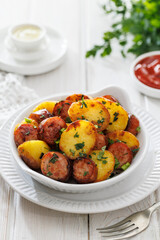 Baked potatoes and sausage slices sprinkled with fresh herbs on a white plate, focus on the middle, close-up