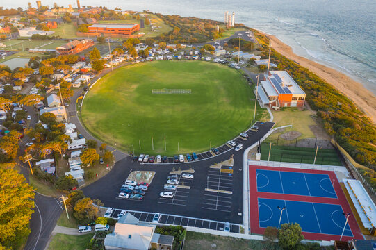 Aerial view of a football oval and netball courts in a caravan park beside the ocean