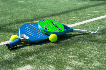 Two padel rackets for children and adults with tennis balls lies on the court, emphasizing action and movement. The dynamic angle captures the energy of an outdoor sports match.