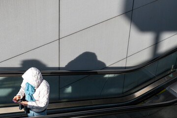 Hooded Person on Escalator Using Smartphone With Strong Shadows
