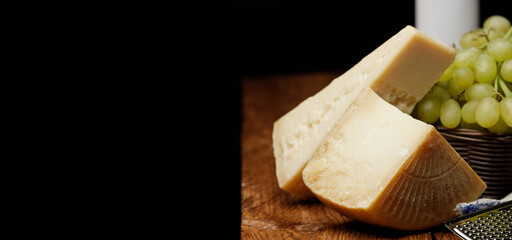 Traditional italian cheeses rodez and parmesan, spaghetti, green grapes in basket and bottle of wine on rustic wooden table on black background