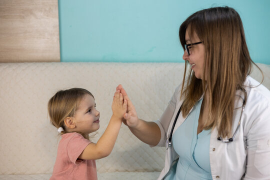 A smiling pediatrician gives a high five to her cute baby after a successful checkup during a home visit creating a trusting relationship between the doctor and the patient Doctor-child relationship.