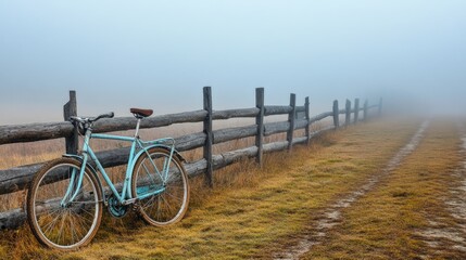Fototapeta premium A touring bicycle resting by a wooden fence with a foggy countryside morning backdrop