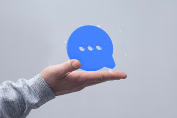 A close-up of a hand holding a floating blue speech bubble icon, symbolizing online messaging or...