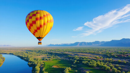 Fototapeta premium vibrant hot air balloon floats gracefully over lush landscape with winding river and distant mountains under clear blue sky