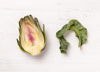 Half of purple raw roman artichokes on a white wooden table top view. Fresh italian vegetables