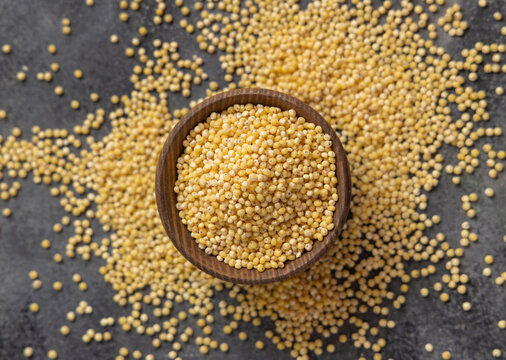 Wooden bowl of raw uncooked yellow pearl hulled millet grain on gray table top view. Ancient food