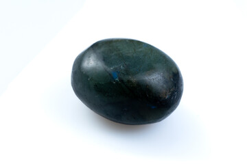 Polished Natural Labradorite Gemstone Showing Colorful Iridescent Blue and Green Flashes on White Surface