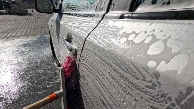 Cleaning a car at a contactless car wash with foam. Washing a car with a brush at a self-service car wash. Slow motion.