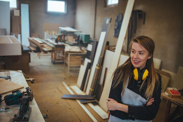 Woman Standing in Workshop with Tools and Materials Around Smiling Confidently