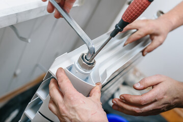 Closeup of plumber installing new hot water central heating radiator at home. New heating battery with a shiny metal nut secured for proper connection and functionality.
