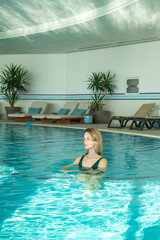 Young woman alone enjoying spending time in indoor swimming pool in the morning. Concept of relaxation and recreation in resort