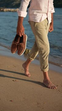 Man walking on the beach with shoes. Vertical footage