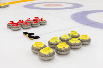 Two sets of curling stones of different colors for two teams, placed near concentric rings on an ice rink