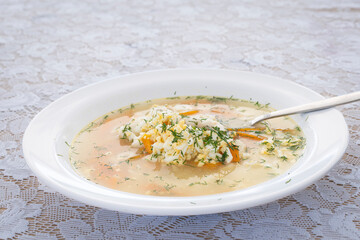 Traditional russian fish soup with greenery. Fish soup with carrots, potatoes and chopped egg. Ukha with perch. Delicious homemade dish in pot on white table. Prepared hot meal with dill.