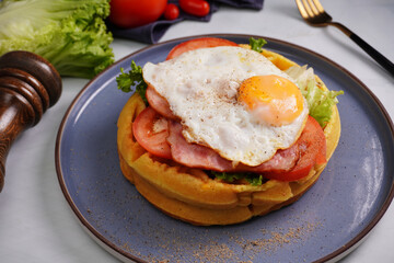 Fresh waffles with fried eggs, lettuce, tomatoes and served for breakfast on a flat table.