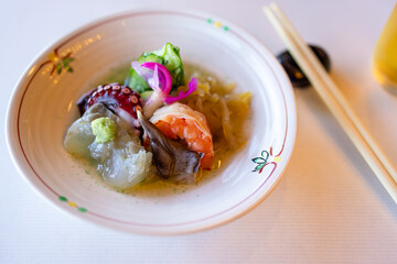 Traditional Japanese appetizer with fresh shrimp, octopus, mollusks, and fermented vegetables, served on a ceramic plate with wasabi and pickled toppings