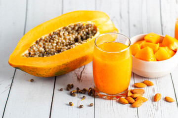 A halved papaya, vibrant smoothie in a glass jar with a straw, fresh cubes in a bowl, and scattered...