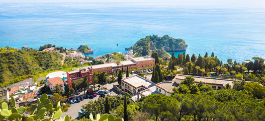Fototapeta premium Panoramic aerial view of picturesque coastline of Taormina in Sicily, Italy with vibrant blue waters of Mediterranean sea, lush greenery and luxury hotels. Welcome to Taormina concept image