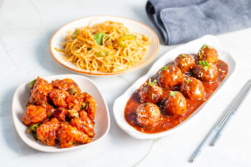 Crispy vegetable Manchurian balls in spicy, tangy sauce, served with stir-fried noodles and crunchy Gobi Manchurian for a flavorful Indo-Chinese feast.