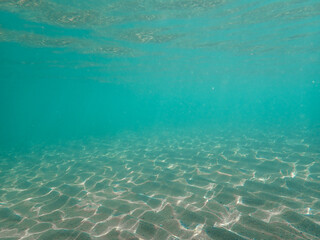 Dark blue ocean surface seen from underwater. Abstract waves underwater and rays of sunlight shining through, Sun light rays undersea deep, Underwater background with sea bottom, Mediterranean sea.