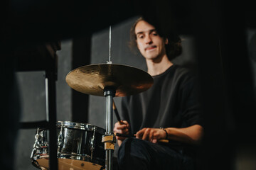 The image shows a drummer playing during a band rehearsal, showcasing focus and practice.