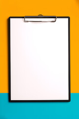 Clipboard with paper clip on colorful background. Clipboard with white clean empty sheet of paper with copy space on yellow and blue background.
