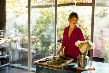 A woman in a cozy home setting prepares fresh vegetables in a sunlit kitchen, surrounded by natural...