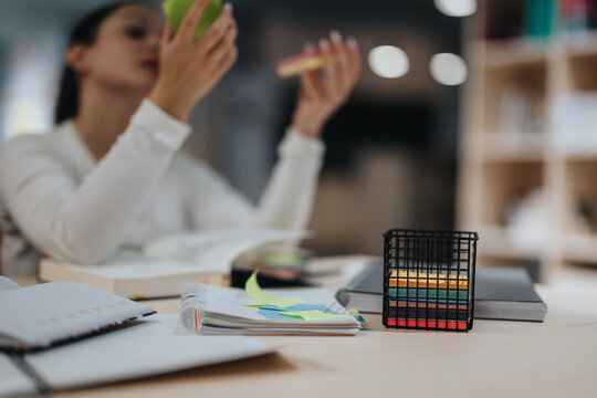 A young woman concentrates on studying at a library table with colorful sticky notes and open books, symbolizing education, organization, and creativity in a modern learning environment.
