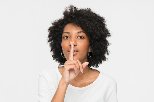 Serious african american woman black girl female afro student holding finger on lips mouth keep it quiet secret information showing hush shh shush gesture isolated on white studio background