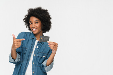 Smiling young african american woman black girl female afro student holding in hand demonstrate pointing index finger of plastic credit bank card isolated on white background. Banking concept