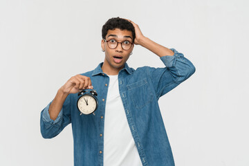 Photo of young African guy male student man amazed shocked hand touch head hold alarm clock late...