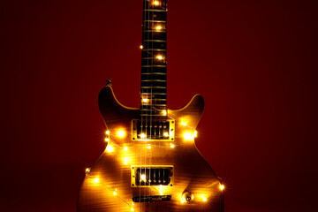Electric guitar with Christmas lights on dark red background, closeup