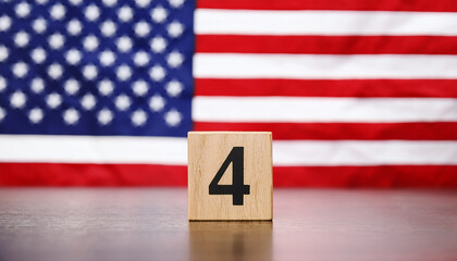 Wooden cube with number 4 on table in front of blurred American flag. The USA.