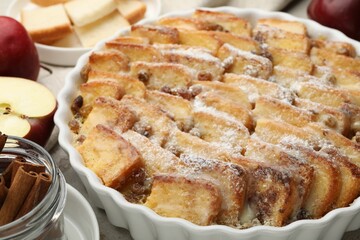 Delicious bread pudding with raisins, powdered sugar, cinnamon and apples on table, closeup