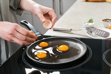 Woman breaking egg into frying pan in kitchen, closeup