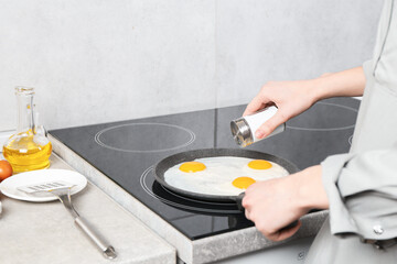 Woman adding salt into frying pan while cooking eggs on cooktop in kitchen, closeup