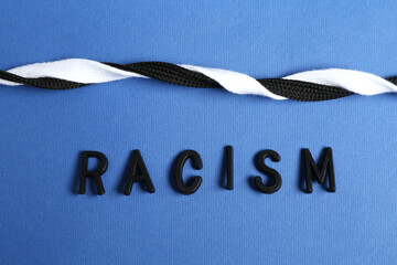 Word Racism and intertwined shoelaces of different colors on blue background, closeup
