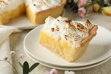 Piece of delicious pie with browned meringue and flowers on light textured table, closeup