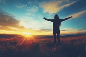 Fototapeta premium A silhouetted figure stands in a field with arms outstretched, facing a vibrant sunset over rolling hills and a colorful sky.