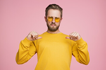 A confident man dressed in yellow points at himself, standing against a pink background. His bold expression and posture suggest pride and self-assuredness, set in a vibrant, modern setting.