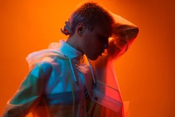 Gardinen Farbenfroh Portrait of a person standing against an orange backdrop, illuminated by dynamic colorful lighting, evoking creativity and modern art aesthetics with contemporary fashion style.  © kegfire
