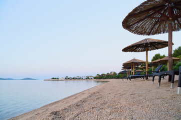 Tranquil beach features straw umbrellas and lounge chairs along the shoreline during twilight hours.