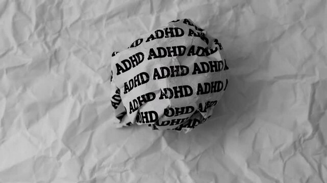 Crumpled paper ball with words ADHD on a crumpled white paper background.