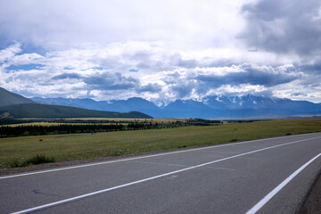 An asphalt road with a white dividing strip against a backdrop of mountain peaks and a beautiful sky. Horizontal photos from traveling. 