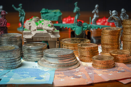 Paris, France - 04 22 2024: View stacks of gold and euros coins, banknotes carpet with soldiers, fighter plane, tank and european flags in background.