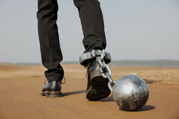 Tired businessman with iron shackles on his legs walks down the road. Bankruptcy, overtime concept.