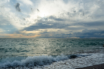 The sound of sea waves crashing on a pebble beach. The setting sun hid behind dark clouds.